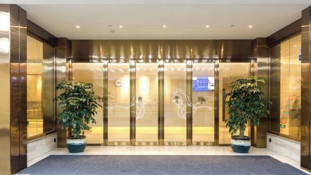 A hotel entrance with a modern design, featuring a glass door with a metallic frame, two potted plants, and a carpeted entrance area. - HanTing Premium Hotel (Xiamen Botanical Garden Bailuzhou Road) (Xiamen)