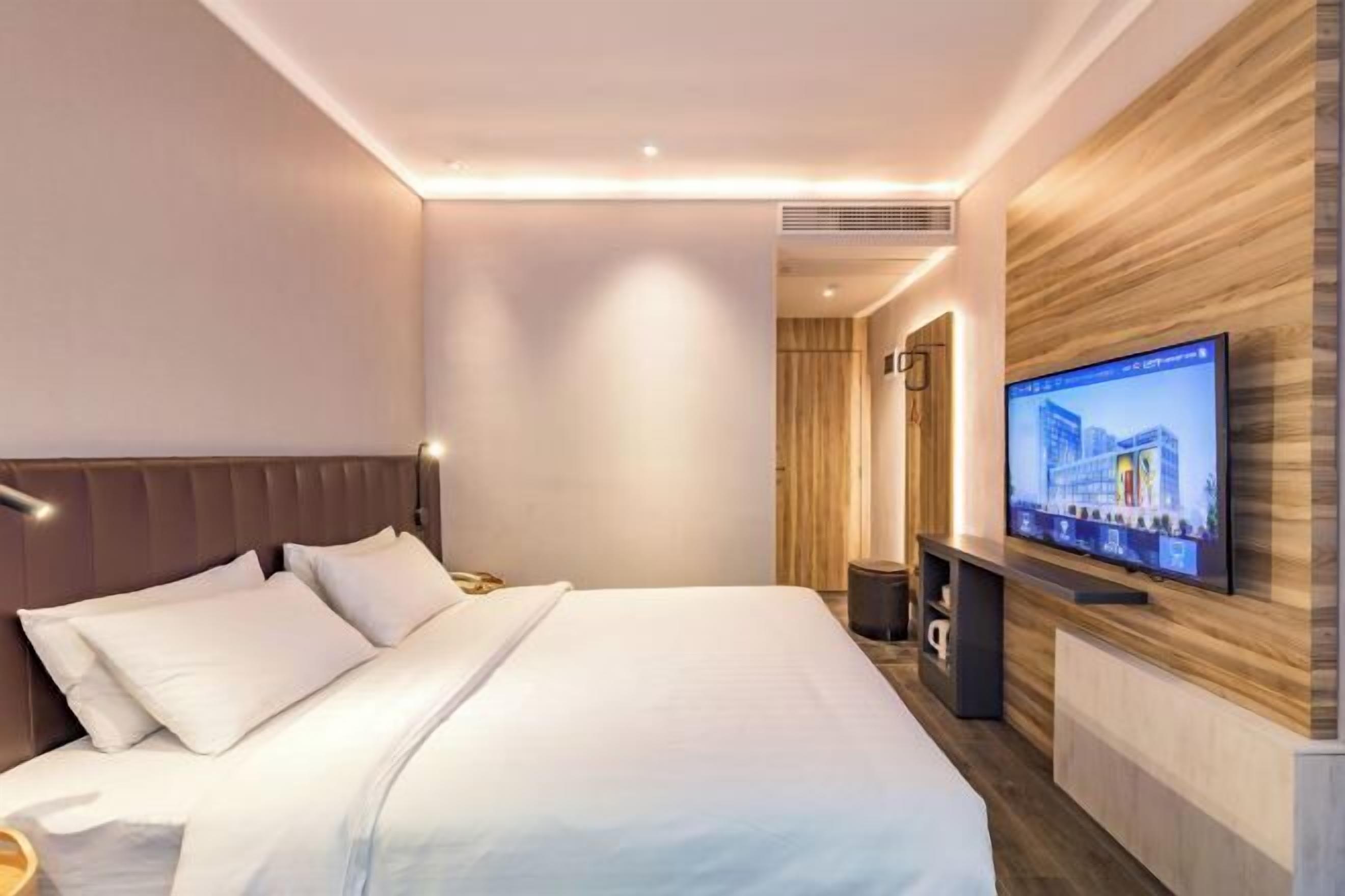 Une chambre d’hôtel moderne dotée d’un grand lit, d’un téléviseur à écran plat fixé au mur et d’un mur décoratif en bois.