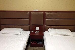 Habitació d'hotel amb dos llits, un capçal, una nitmul i un espai per guardar sabates.