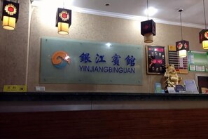 Una zona de recepció amb un cartell que diu 'YINJIANGBINGUAN', un rellotge digital i una estàtua daurada.