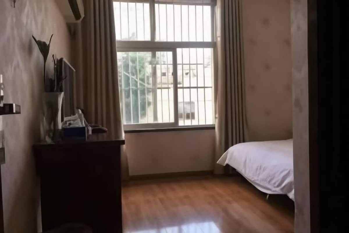 Une pièce comprenant un lit, une fenêtre avec des rideaux, un bureau avec une lampe et une étagère fixée au mur.