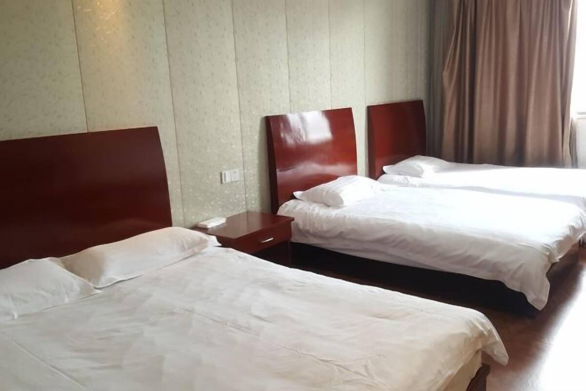 Une chambre d’hôtel avec deux lits simples, des têtes de lit en bois, une table de chevet et une fenêtre avec des rideaux.