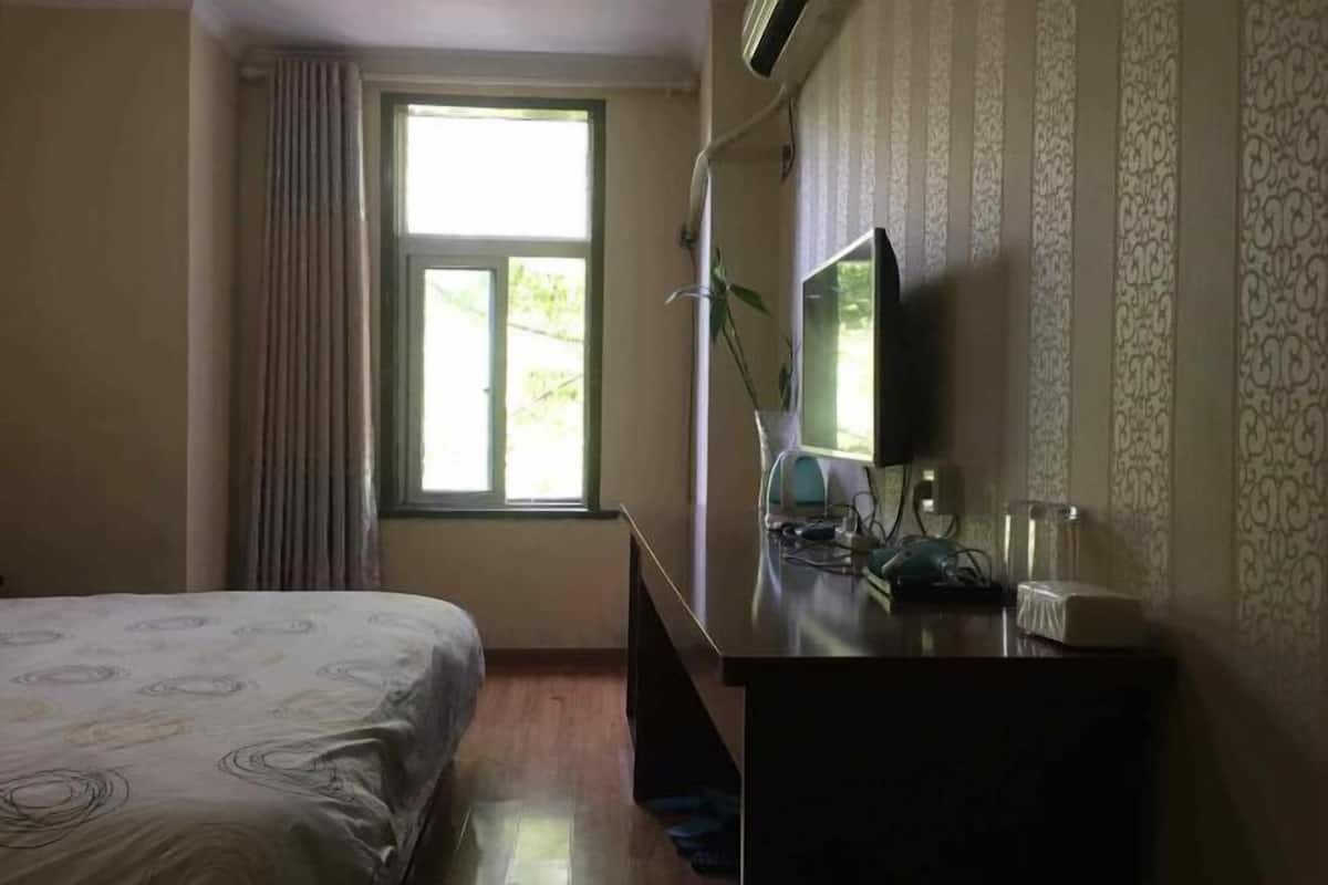 Une chambre d’h ôtel équipée d’un lit, d’un bureau avec un ordinateur, d’une fenêtre avec des rideaux et d’un climatiseur fixé au mur.
