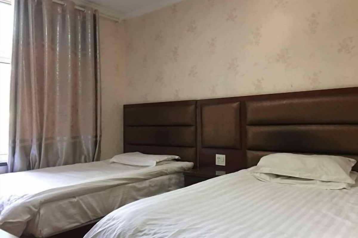 A hotel room with two single beds, a wooden headboard, and a window with curtains.