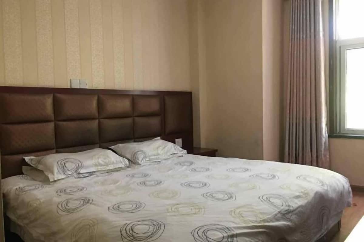 Une chambre d’hôtel avec un grand lit, une tête de lit et une fenêtre avec des rideaux.