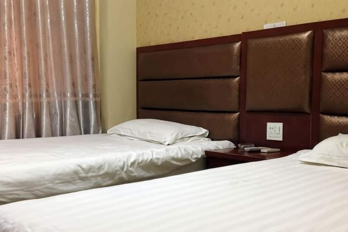 Une chambre d’hôtel avec deux lits, une tête de lit en bois, une table de chevet et une fenêtre avec des rideaux.