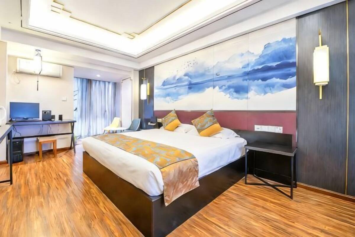 A hotel room with a large bed, a desk, a chair, and a painting on the wall.