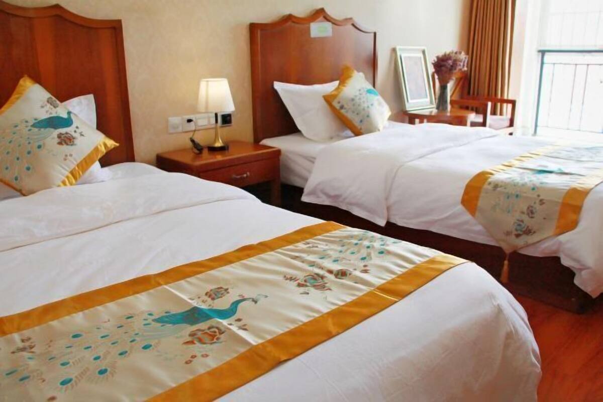 A hotel room with two beds, each with white bedding and decorative pillows. There is a nightstand with a lamp and a framed picture.