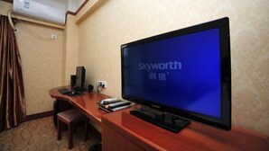 A hotel room with a large flat-screen TV, a wooden desk, a chair, and an air conditioning unit on the wall. - Jingshiji Express Hotel (Jinghong)