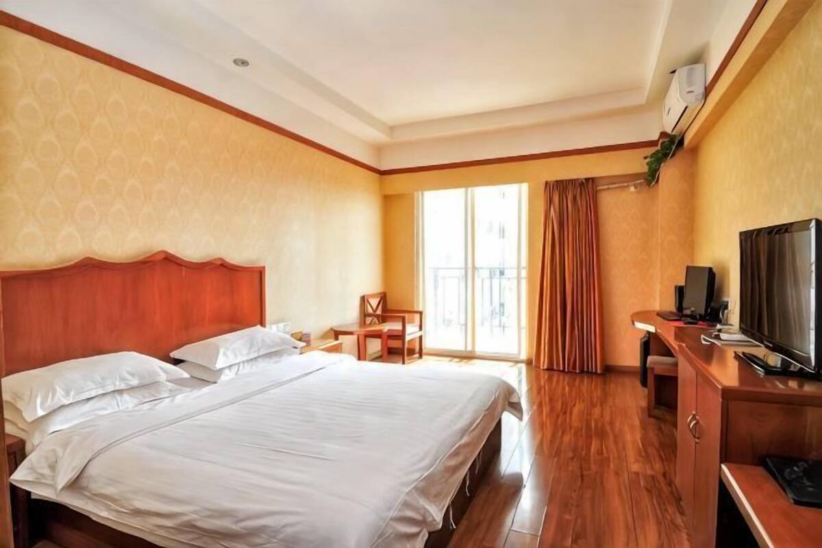 A hotel room with a large bed, a desk with a TV, a chair, and a window with curtains.