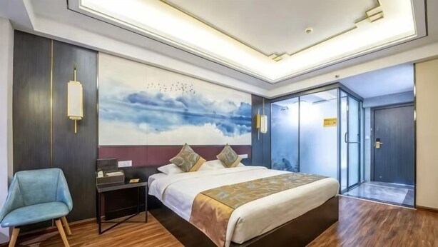 A hotel room with a large bed, a desk, a chair, a nightstand, and a wall with a painting. - Jingshiji Express Hotel (Jinghong)