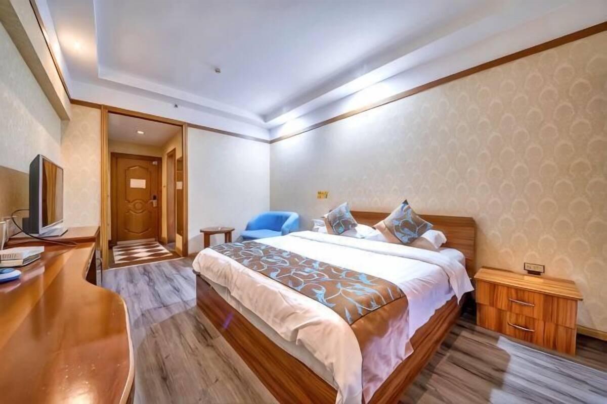A hotel room with a wooden bed, a desk with a chair, a television, and a door leading to another room.