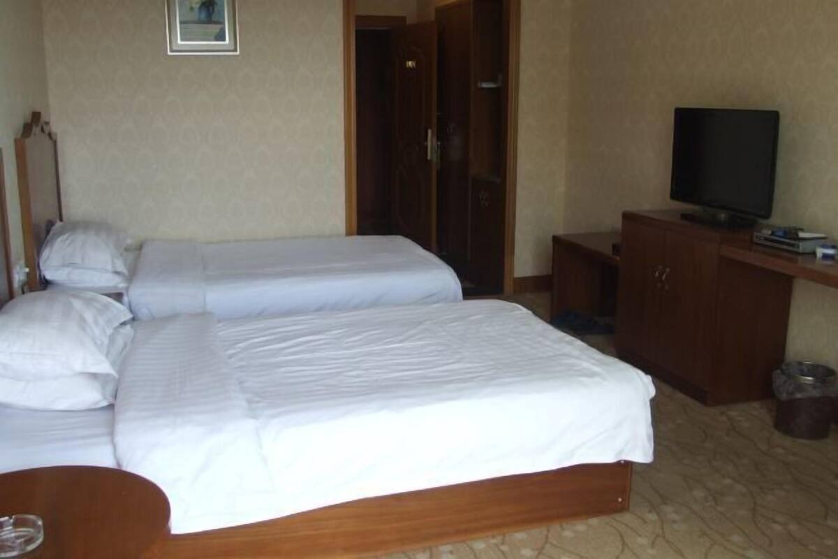 A hotel room with two beds, a TV, a wooden cabinet, and a door.