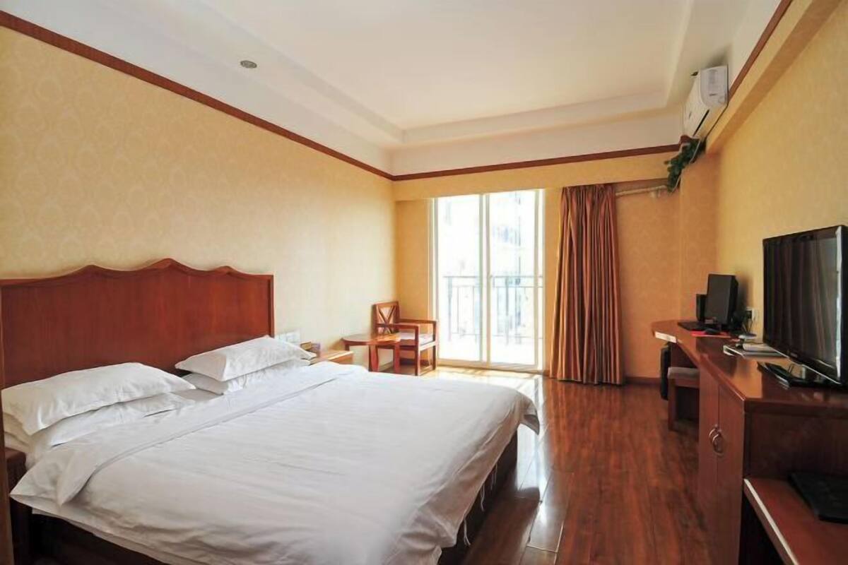 A hotel room with a large bed, a desk with a TV, and a window with curtains.