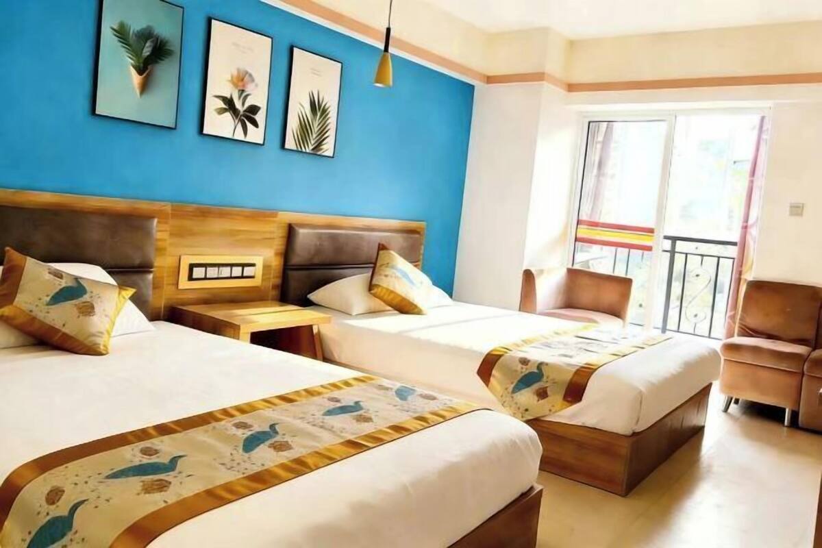A hotel room with two beds, a wooden headboard, a nightstand, a chair, and a balcony with a view.