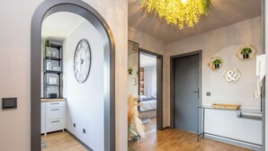 A modern interior with a wooden floor, a kitchen area with cabinets and a clock, and a hallway leading to a bedroom. - Modern apartment with balcony & 2 parking spaces (Odenthal)