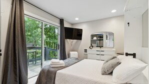 Moderni hotellihuone, jossa on suuri sänky, taulutelevisio, minibaari ja liukuovi, joka johtaa ulos.