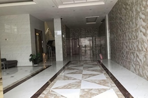 Un vestíbulo amplio con piso de mármol, puerta de cristal de acceso y una escalera que sube a los niveles superiores.