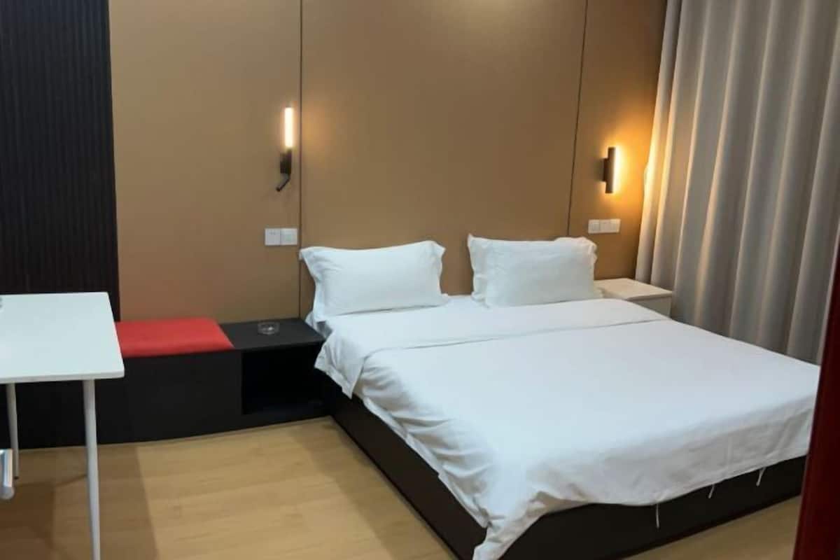 A hotel room with a bed, bedside tables, a small table, and a red bench.