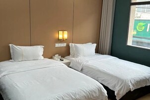 Habitación de hotel con dos camas, una mesita de noche con un teléfono y una lámpara, y una ventana con vista a un edificio.