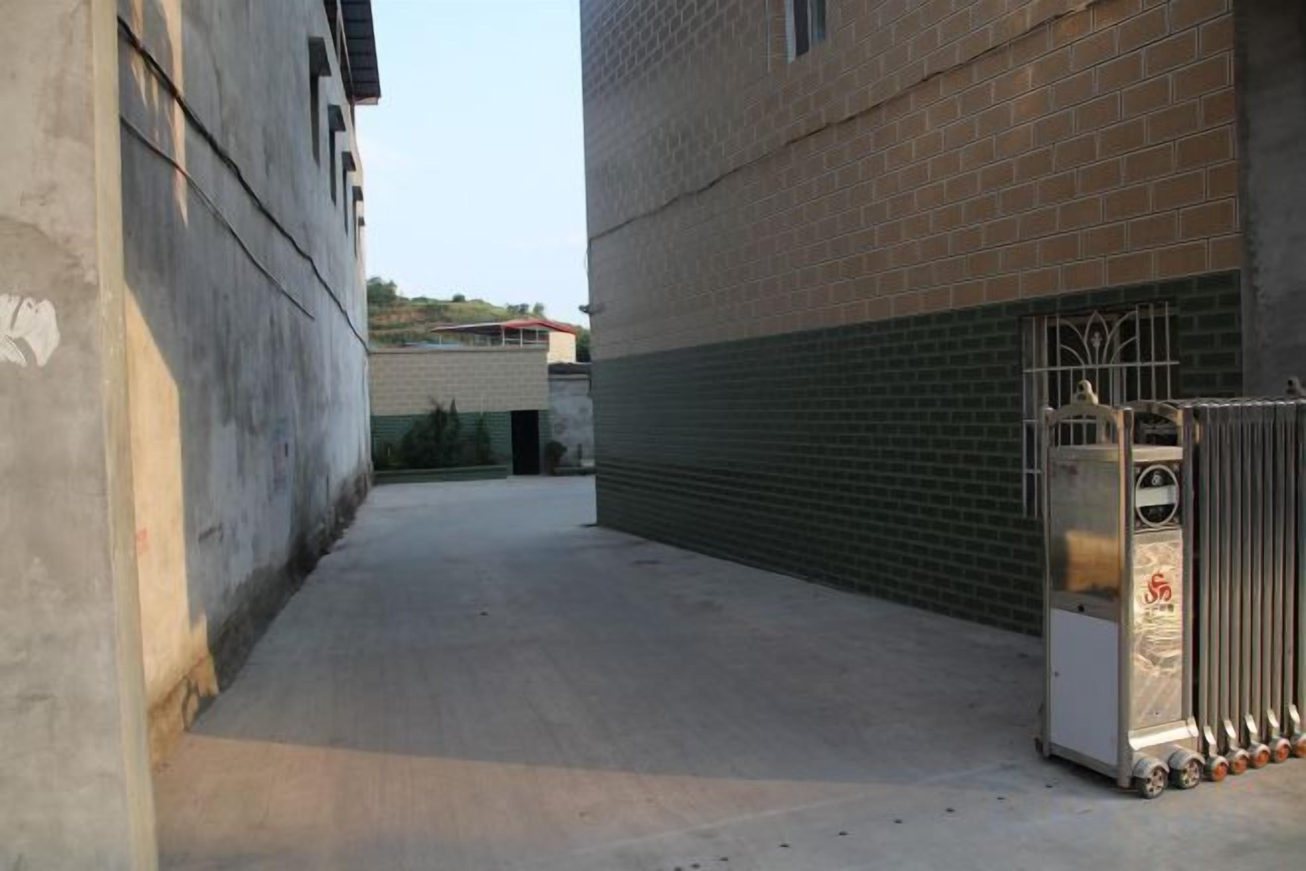 A narrow alleyway with a concrete floor, a metal gate, and a brick building with a metal shutter.