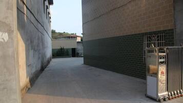 A narrow alleyway with a concrete floor, a metal gate, and a brick building with a metal shutter.