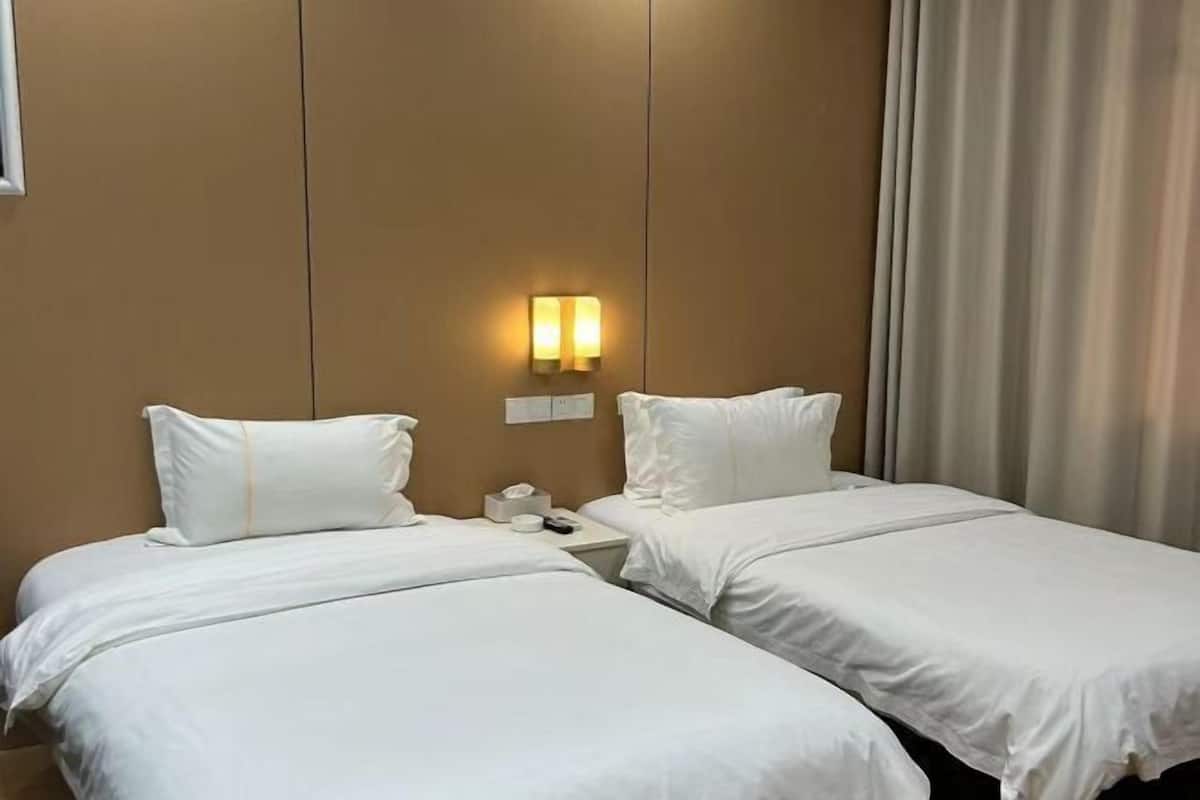 A hotel room with two beds, a nightstand, a wall-mounted light, and a window with curtains.