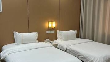 A hotel room with two beds, a nightstand, a wall-mounted light, and a window with curtains.