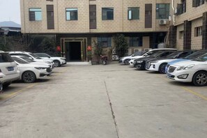 A parking lot with several cars parked in front of a building with multiple windows and a door. - Zhongjiang Fengshang Hotel (Zhongjiang)