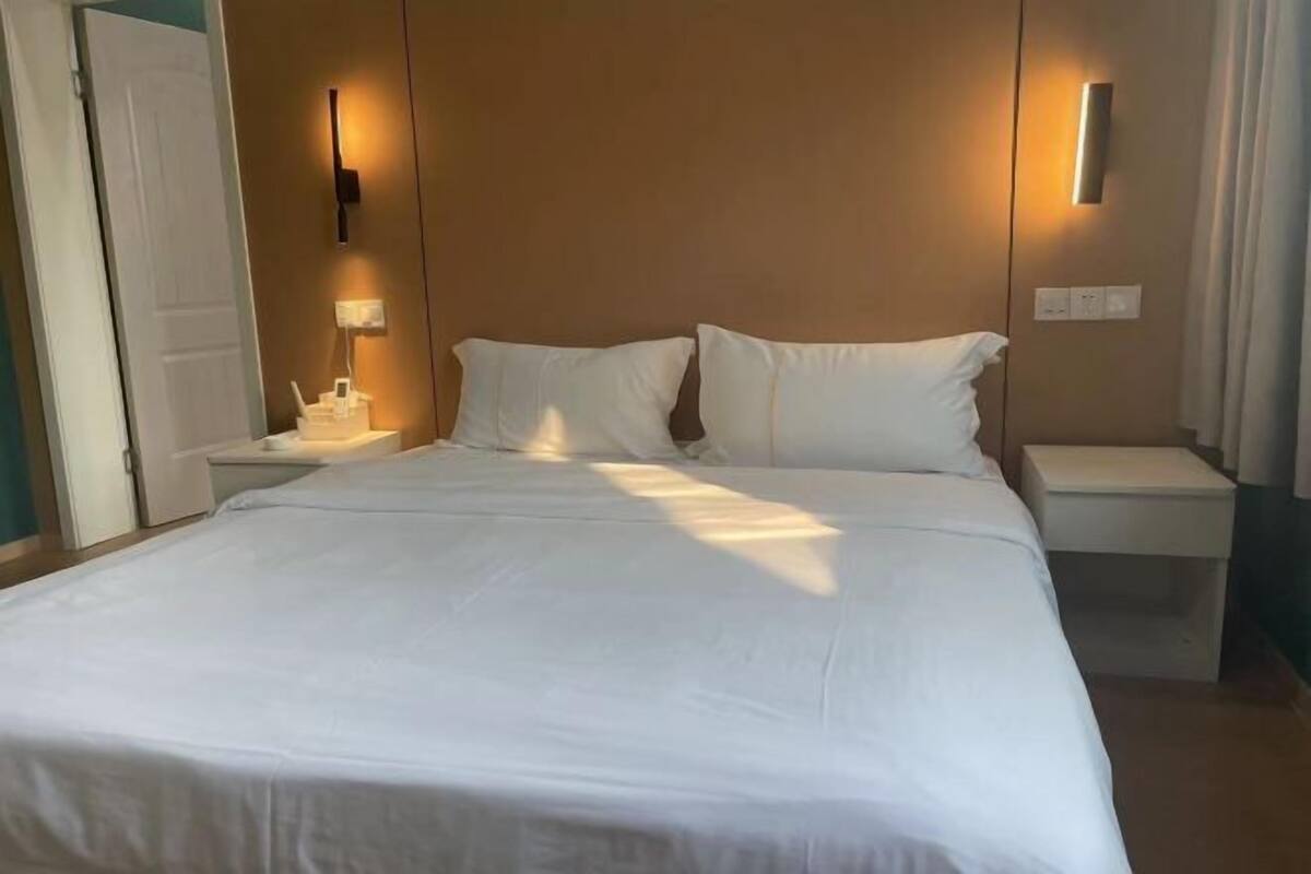 A hotel room with a large bed, two bedside tables, a nightstand, and a wall-mounted light fixture.