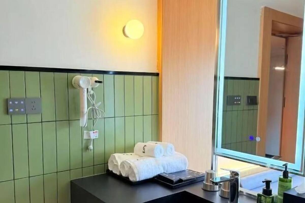 A hotel bathroom with a green tiled wall, a towel rack, a sink, and a mirror.