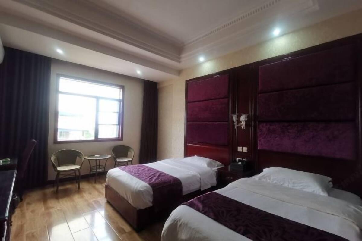 A hotel room with two beds, a large window, and a seating area with chairs.