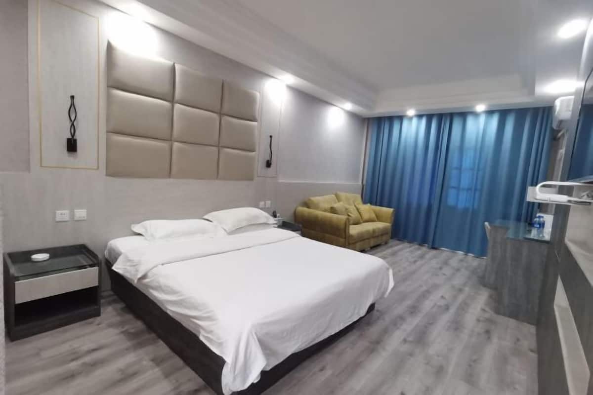 A modern hotel room with a large bed, a bedside table, a sofa, a desk, and a mirror.