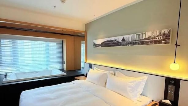 A hotel room with a bed, a window with blinds, a wall-mounted picture, and a bedside table with a lamp. - Zhongjiang Fengshang Hotel (Zhongjiang)