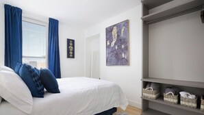 A bedroom with a bed, blue curtains, a white wall, and a grey wardrobe.