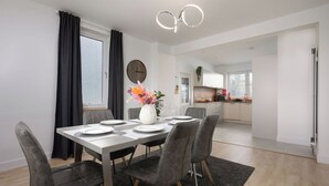 A modern dining area with a white table set for four, grey upholstered chairs, a dark rug, and a vase with flowers.
