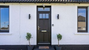 A white building with a black door, two potted plants, and a small window on the right.
