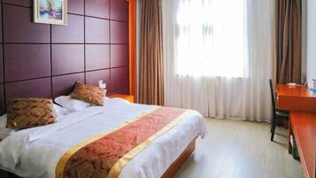 A hotel room with a bed, a desk, a chair, a painting on the wall, and a window with curtains.