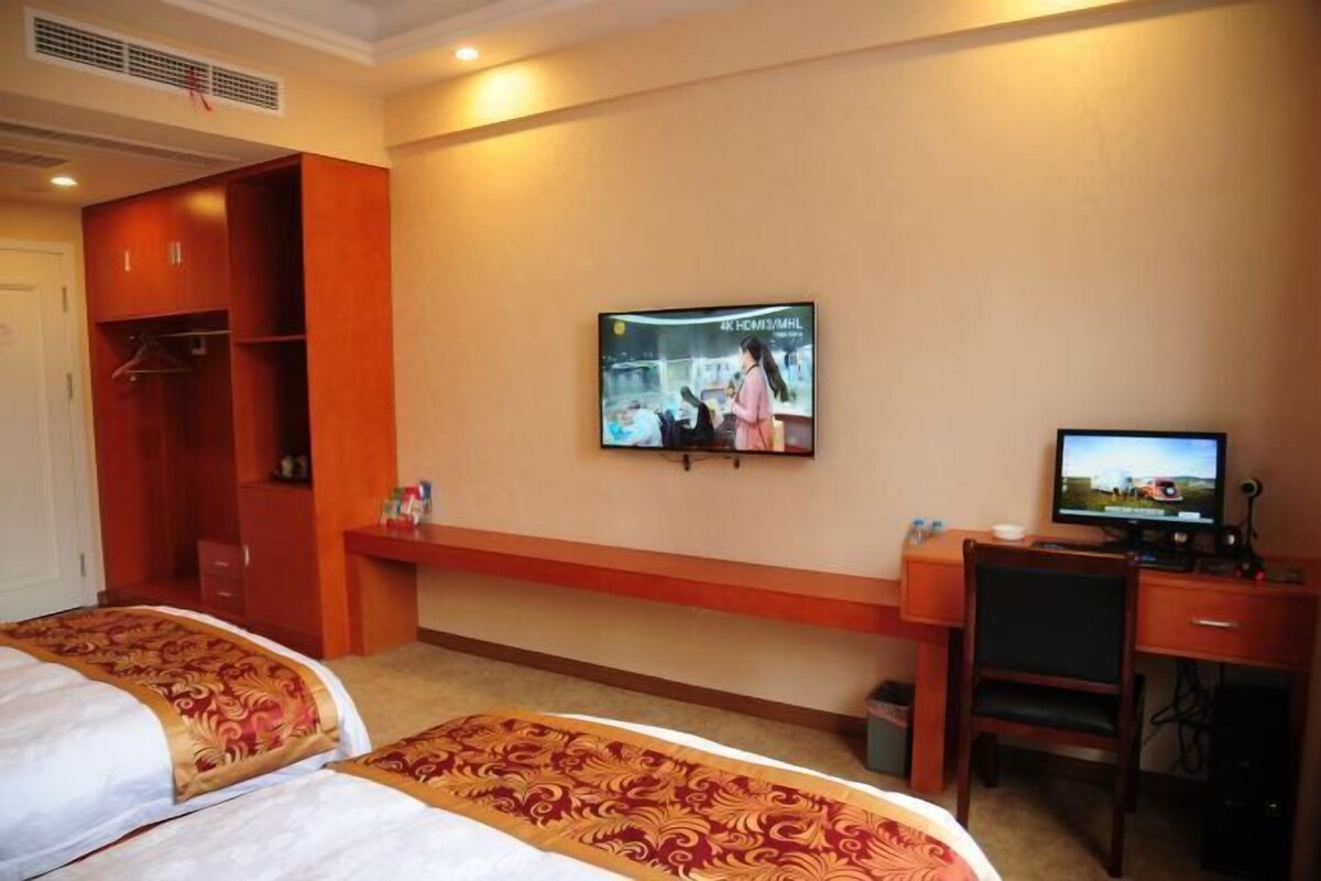 A hotel room with two beds, a desk, a television, and a wardrobe.
