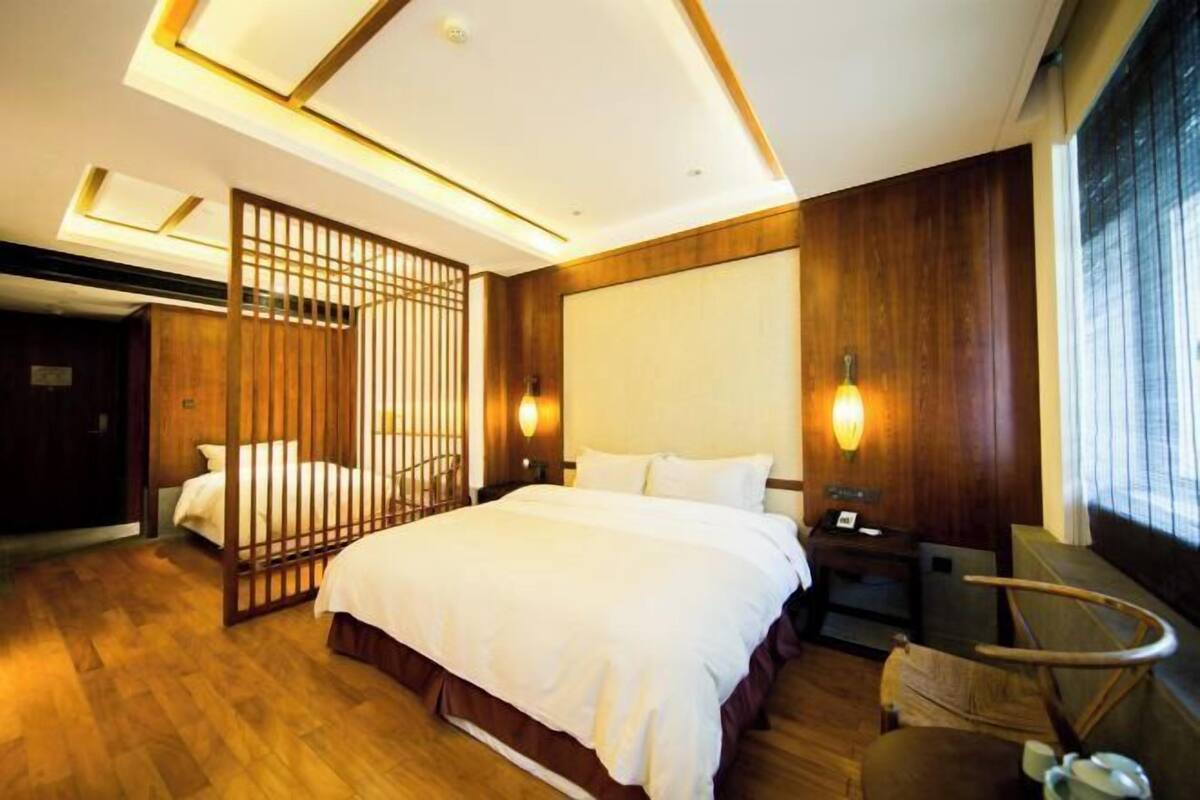 A hotel room with a large bed, wooden paneling, a desk with a chair, and a window with blinds.