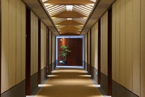 A corridor with a wooden ceiling, a plant, and a door at the end. - Ruyi Resort · International Cultural Center of Buddhism, Putuoshan (Zhoushan)