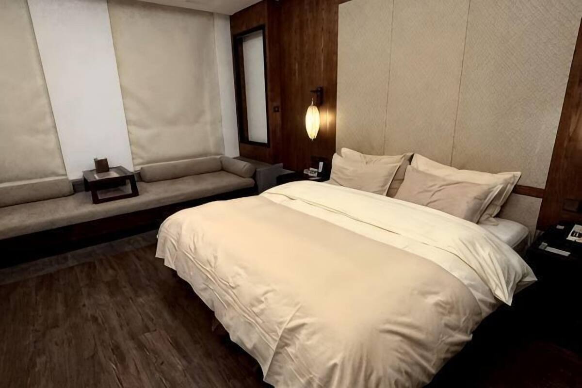 A hotel room with a bed, a bench, a nightstand, and a wall-mounted light fixture.