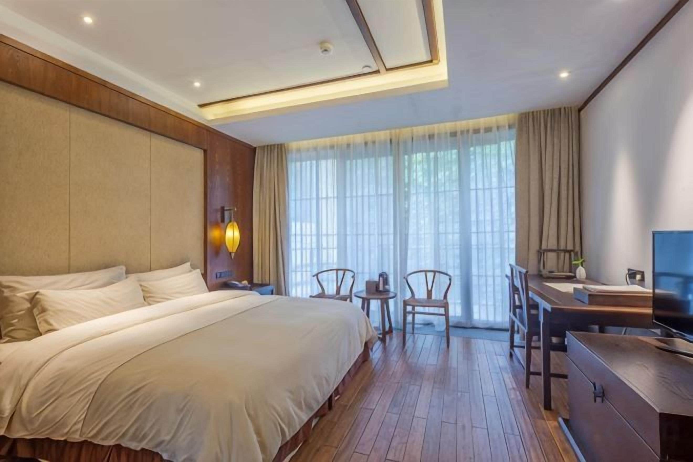 Ein Hotelzimmer mit einem großen Bett, einem Schreibtisch, einem Sessel, einem Fernseher und einem Fenster mit Vorhängen.