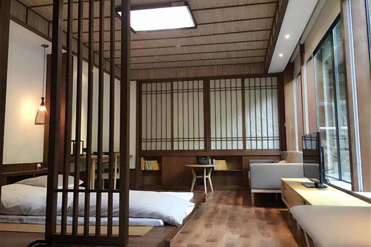 A hotel room with a wooden floor, a bed, a desk, a chair, and a TV.