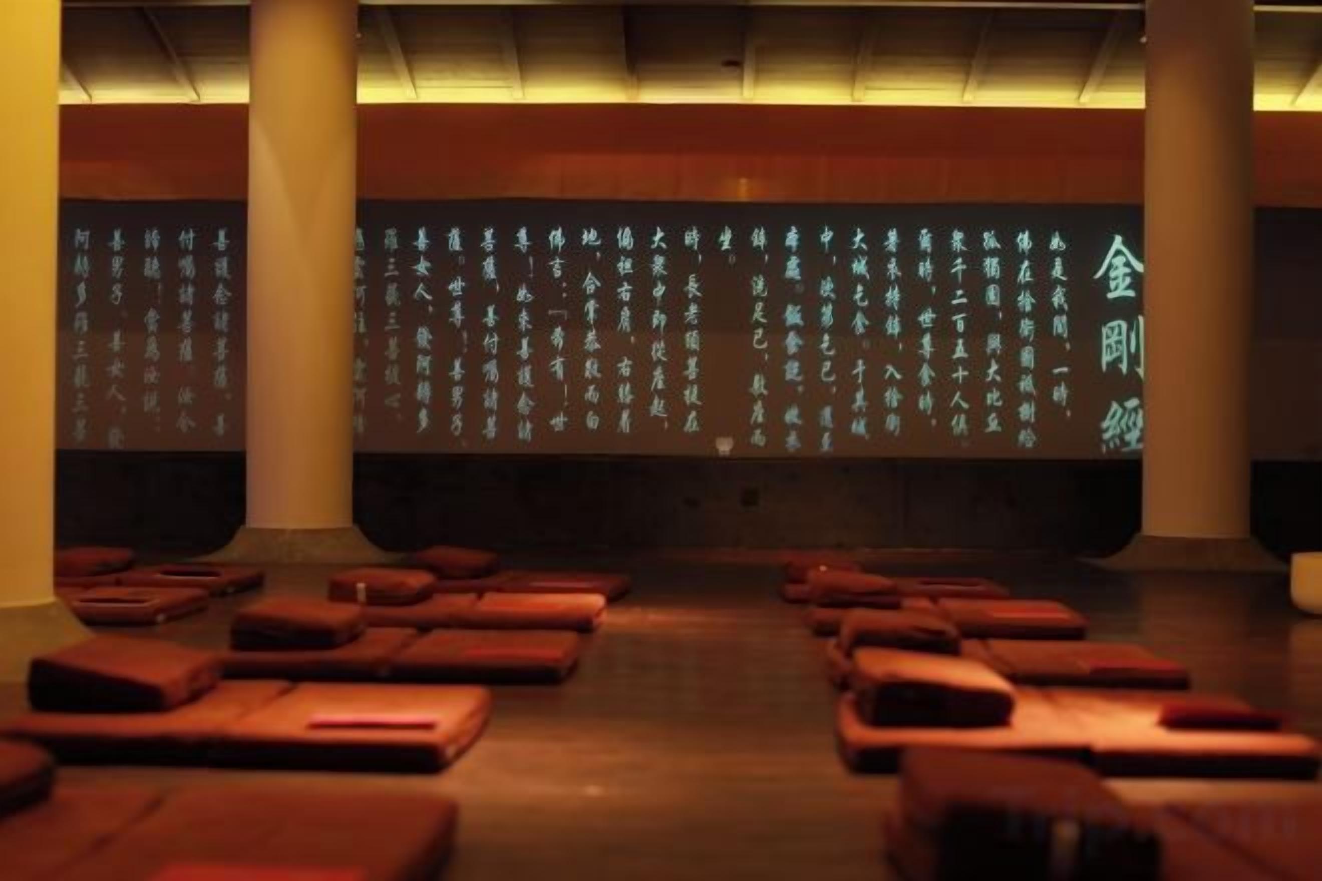 A room with rows of wooden benches and a projection screen displaying text.