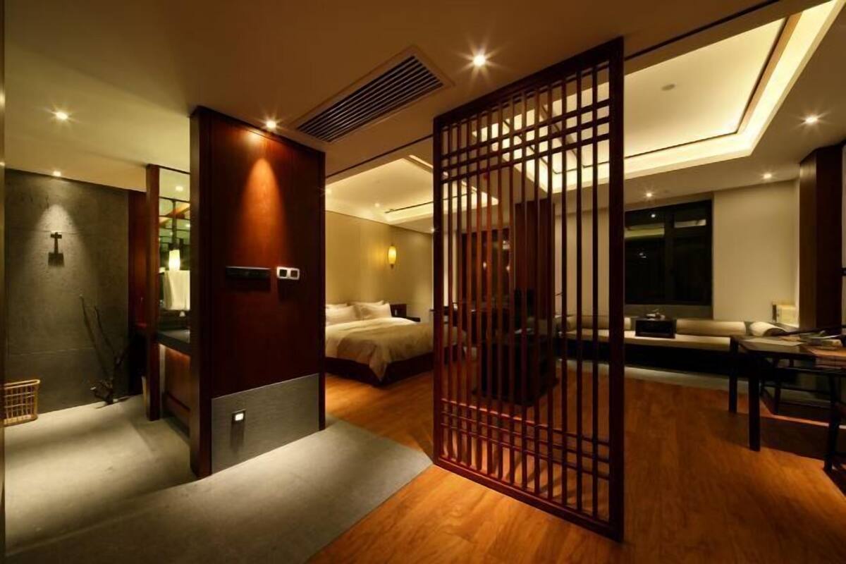 A modern hotel room with a large bed, a desk, a seating area, and a view of the city at night.
