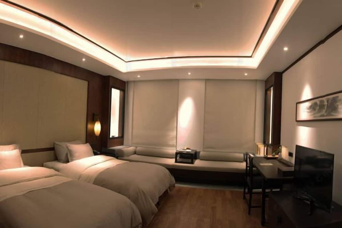 A modern hotel room with two beds, a seating area, a desk with a chair, and a TV.