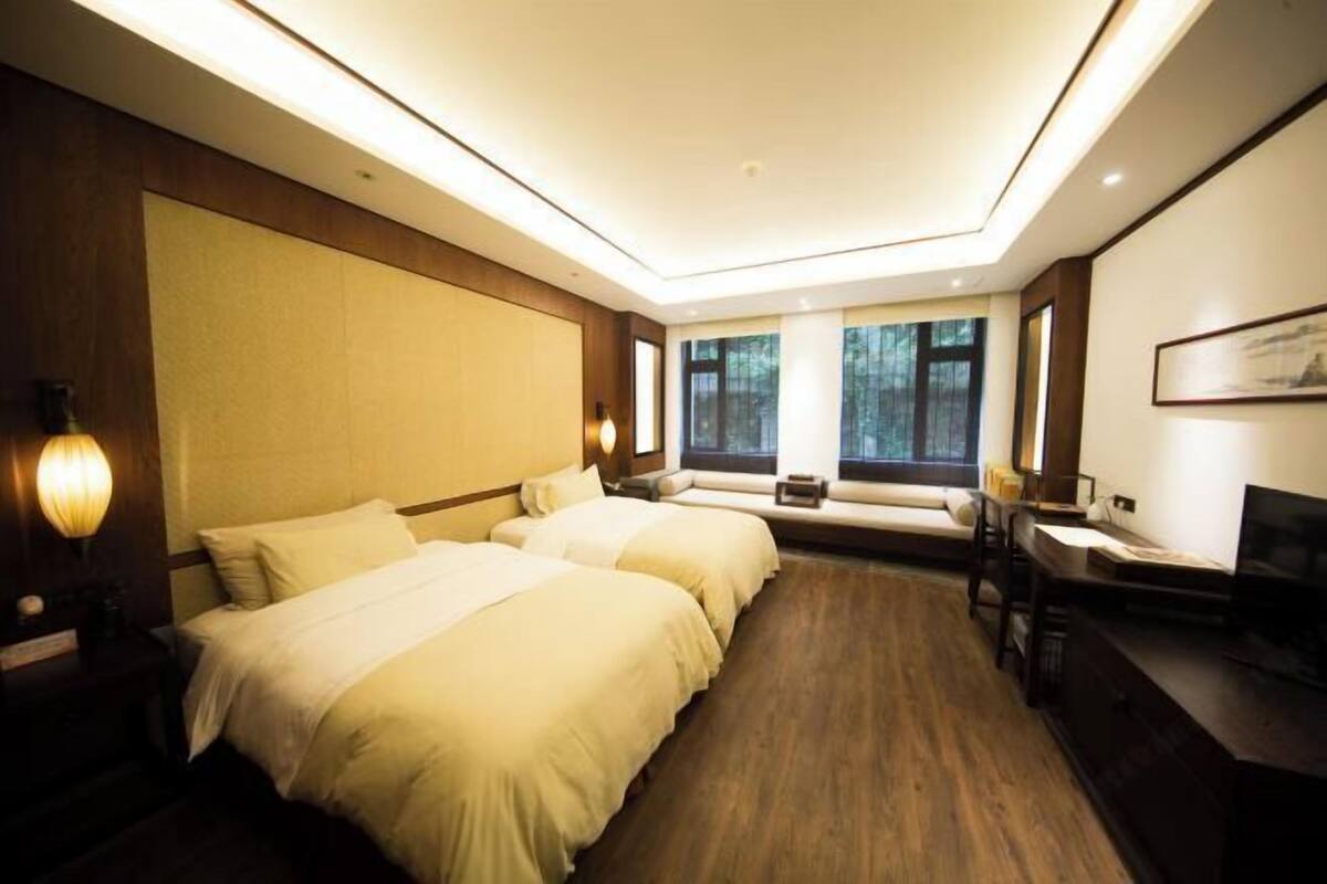 A hotel room with two beds, a desk, a TV, and large windows.