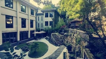 Une cour bordée d’un mur en pierre, un petit jardin et un bâtiment doté de grandes fenêtres.