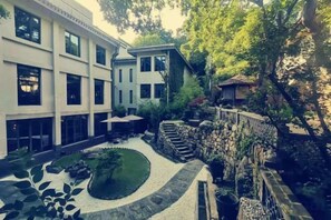 Un cortile con un muro in pietra, un piccolo giardino e un edificio con ampie finestre.